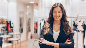 Young female retailer looking at the camera smiling with retail fashion shop in the background